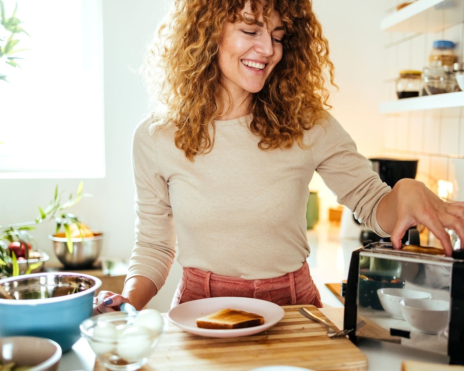 Mujer sonriendo mientras prepara el desayuno, refleja energía positiva y bienestar natural – Un Aceite Para Eso