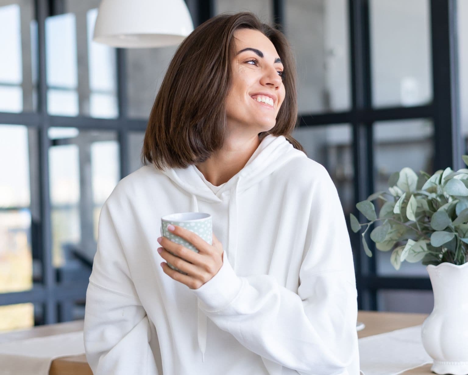 Mujer tranquila en casa sosteniendo una taza, representando el uso de aceites esenciales para regular hormonas y apoyar el equilibrio femenino.